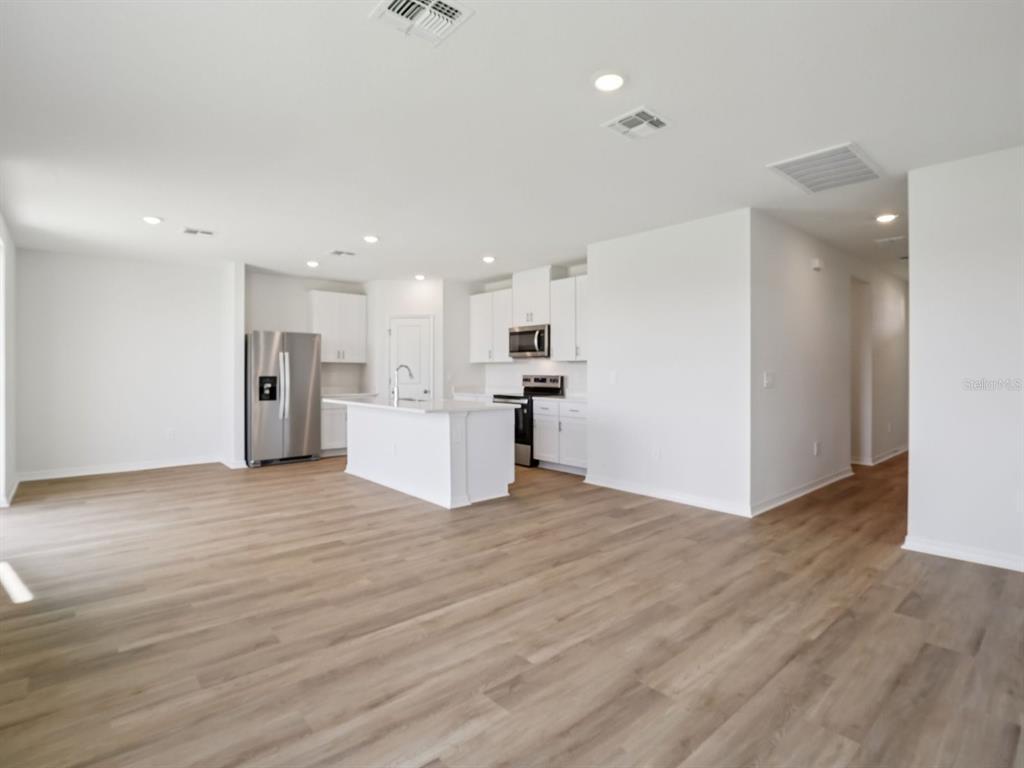 An open-concept kitchen with white cabinets, stainless steel appliances, and light wood-look flooring — 11316 BELLEWOOD TERRACE, PARRISH, FL