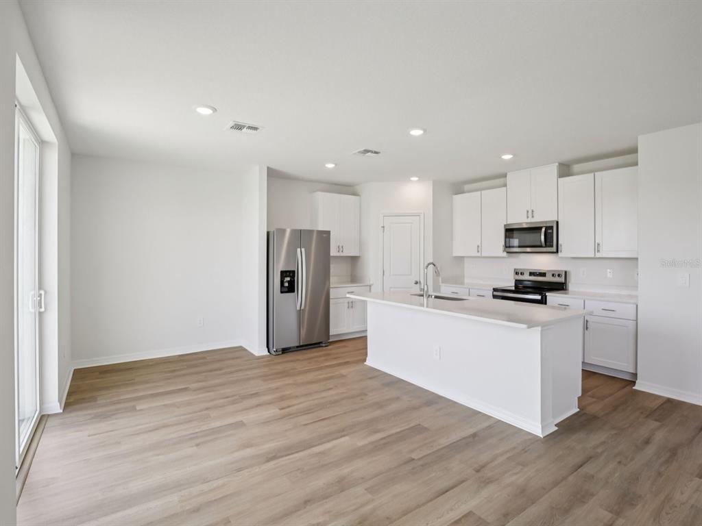 A modern kitchen features white cabinets, stainless steel appliances, and a central island with seating — 11316 BELLEWOOD TERRACE, PARRISH, FL