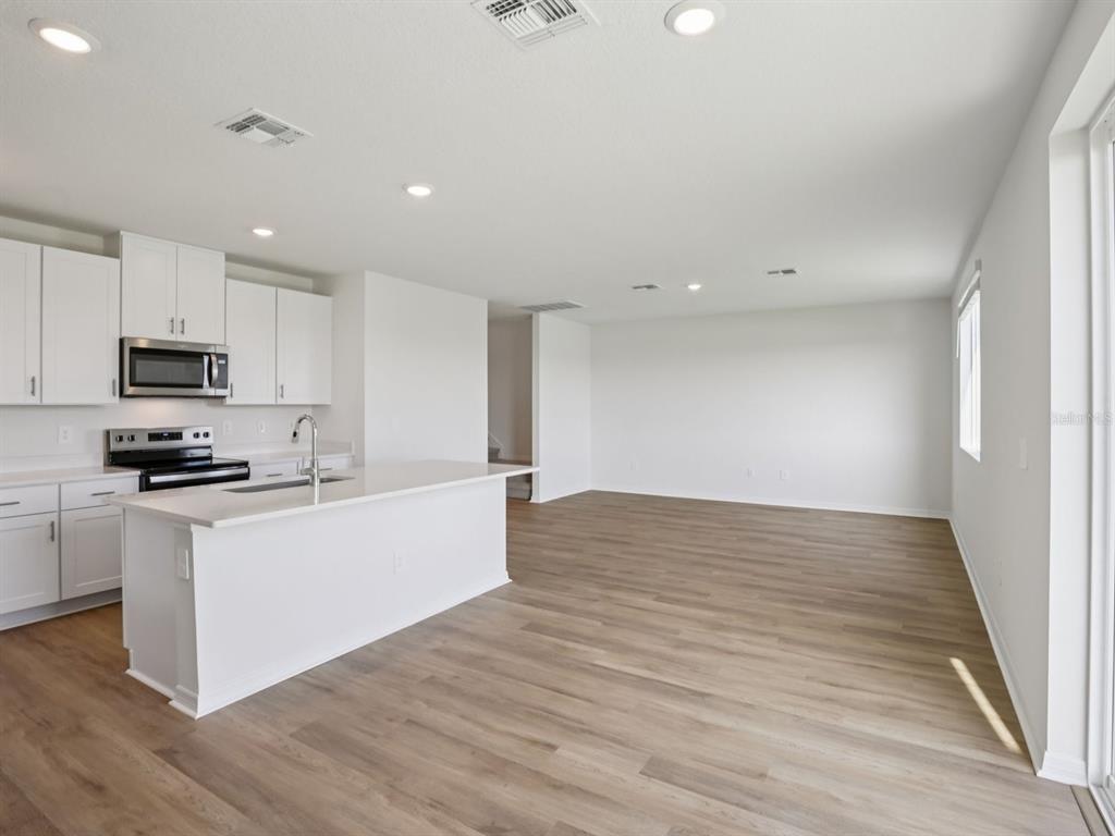 A modern kitchen with white cabinets and an island opens into a spacious living area — 11316 BELLEWOOD TERRACE, PARRISH, FL