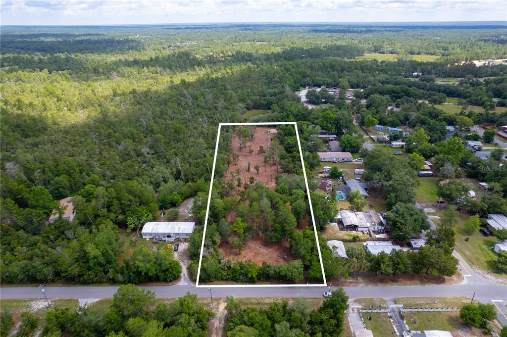 An aerial view shows a rectangular, partially wooded vacant lot outlined in white — DIVISION STREET, DELAND, FL