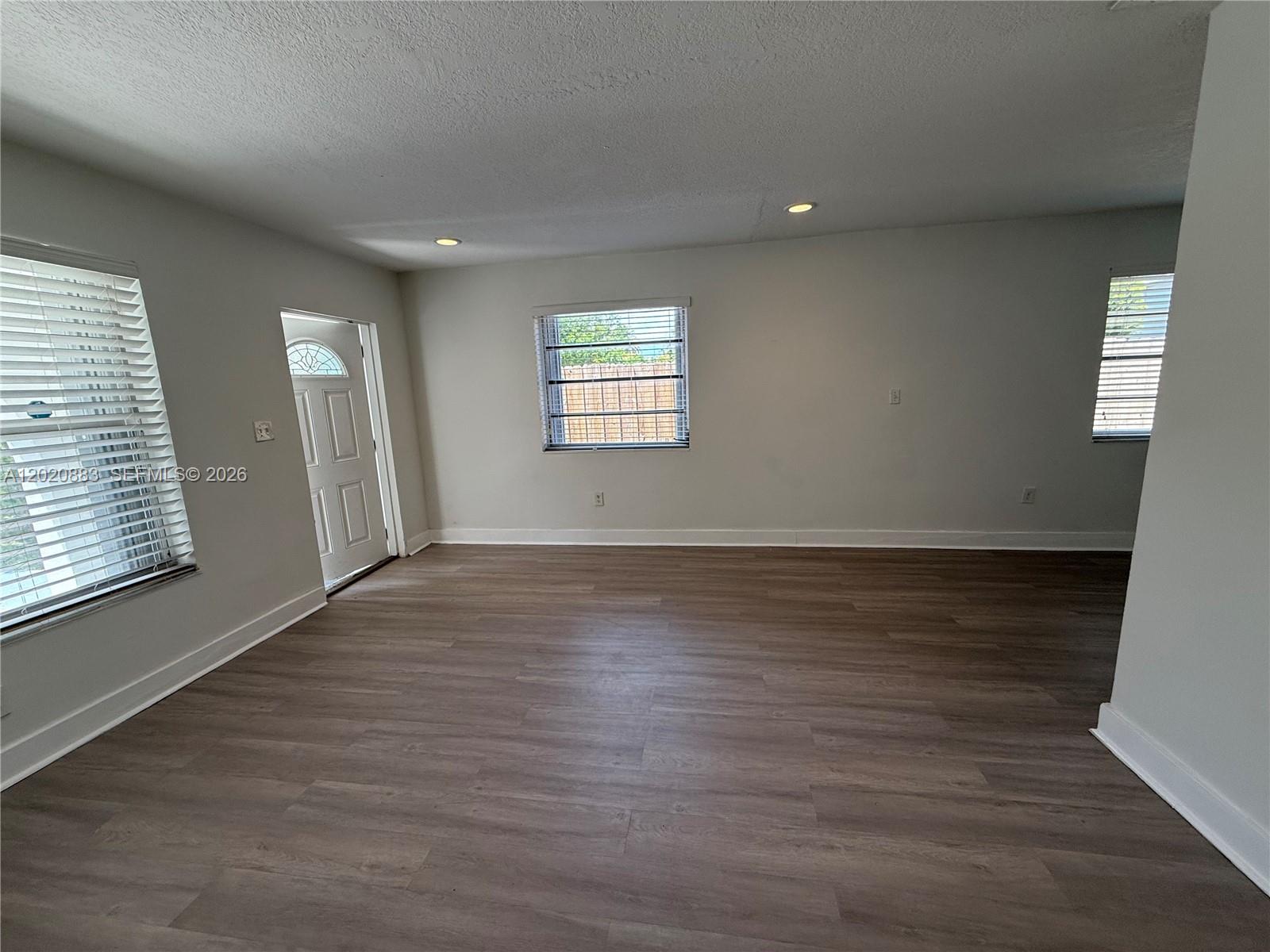 An empty room features light gray walls, wood-look flooring, recessed lighting, and three windows — 1809 NW 33rd St # 1809, Miami FL 33142, MIAMI, FL
