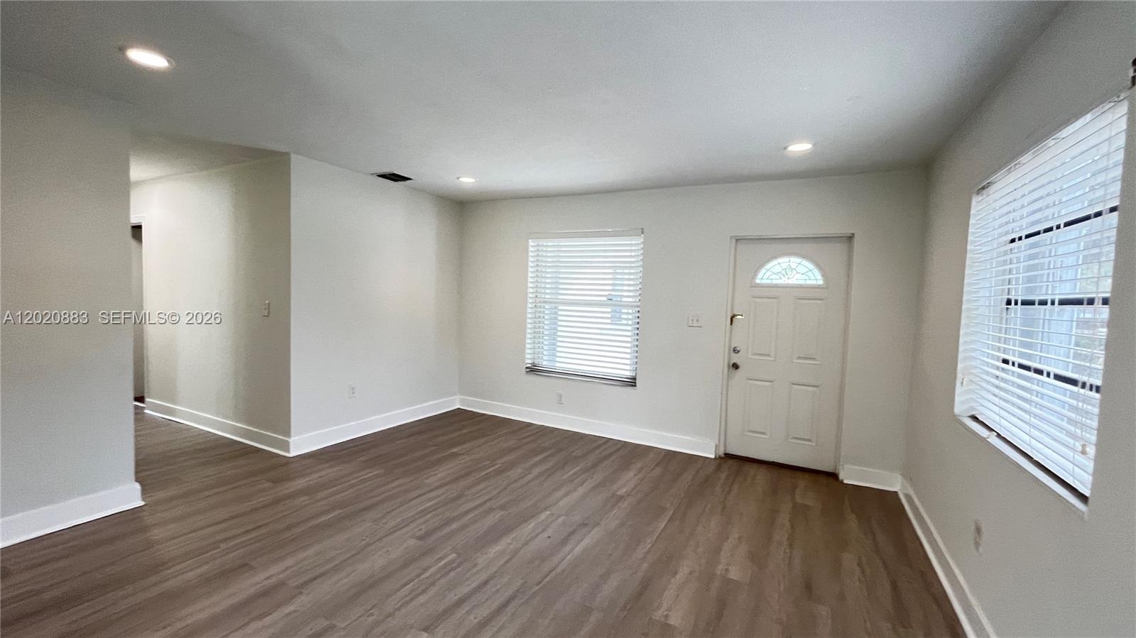 An empty living room features light gray walls, wood-look flooring, recessed lighting, and two windows — 1809 NW 33rd St # 1809, Miami FL 33142, MIAMI, FL