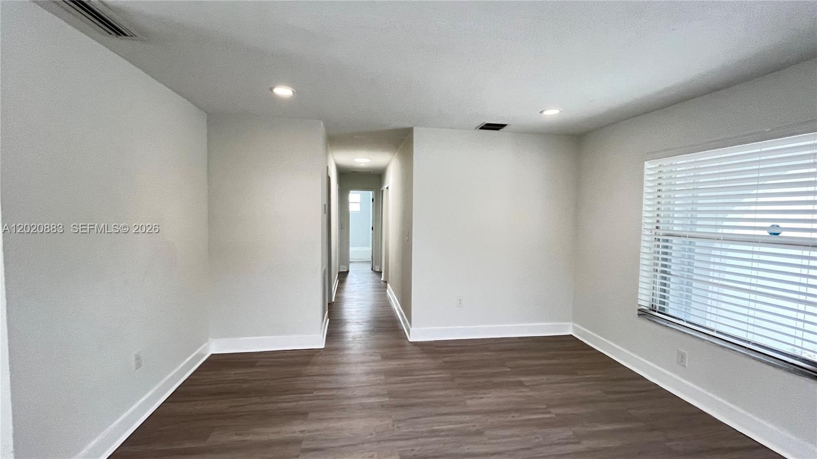 An empty room features light gray walls, wood-look flooring, and a hallway leading further inside — 1809 NW 33rd St # 1809, Miami FL 33142, MIAMI, FL