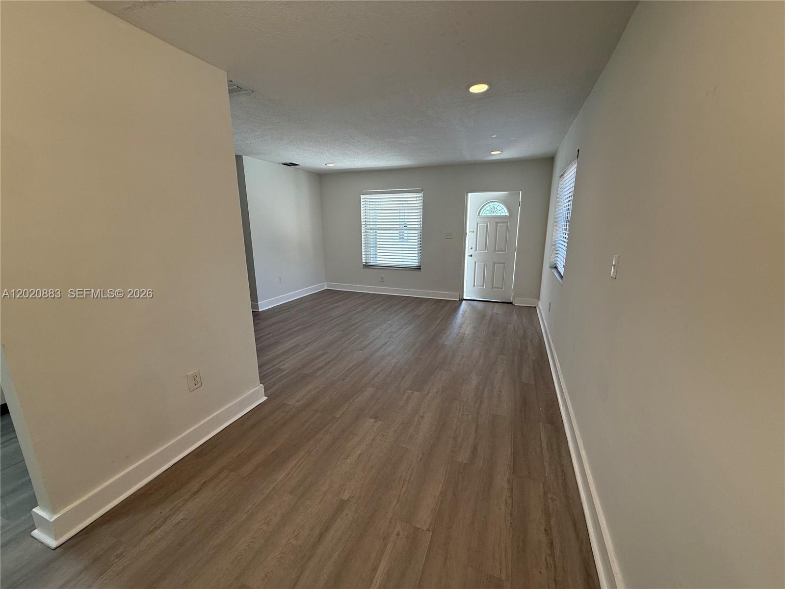 An empty living room features light gray walls, wood-look flooring, recessed lighting, and a front door — 1809 NW 33rd St # 1809, Miami FL 33142, MIAMI, FL