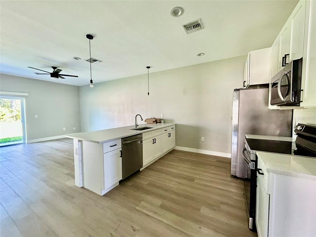 A kitchen features white cabinets, stainless steel appliances, a center island, and light wood flooring — 12552 BUFFING ROAD, PORT CHARLOTTE, FL