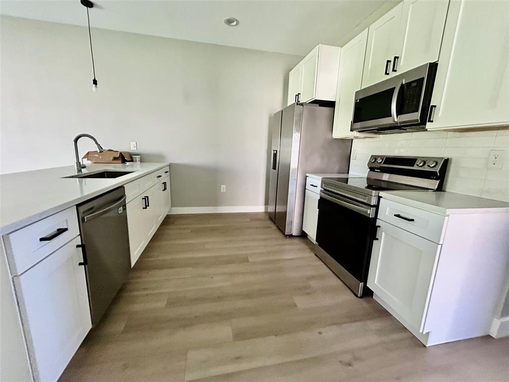 A kitchen features white cabinets, stainless steel appliances, and light wood-look flooring — 12552 BUFFING ROAD, PORT CHARLOTTE, FL