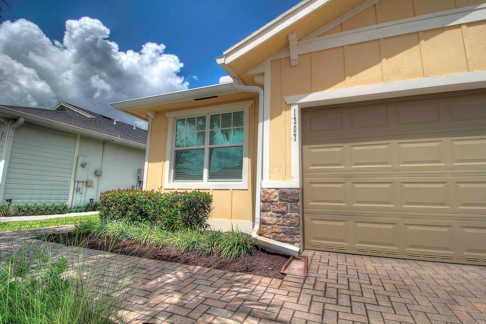 A yellow house exterior features a tan garage door, a window, and a stone facade — 1307 Tangled Orchard Trace, Loxahatchee FL 33470, LOXAHATCHEE, FL