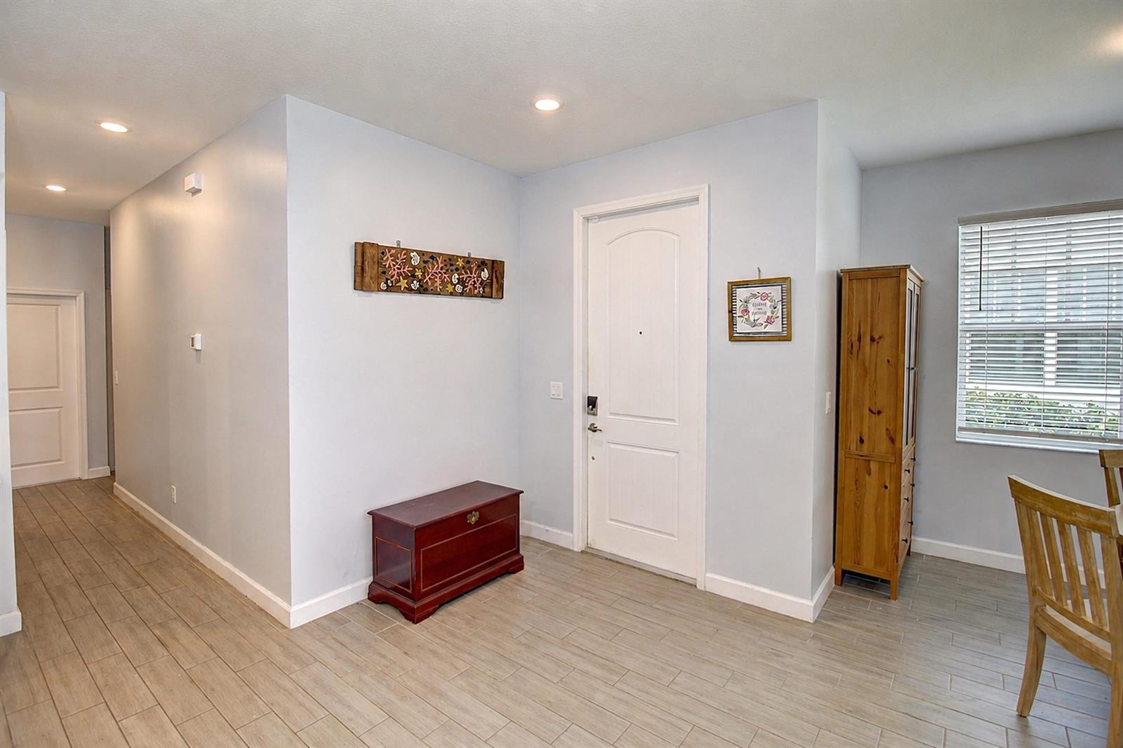 An entryway features light blue walls, wood-look tile flooring, a wooden chest, and a front door — 1307 Tangled Orchard Trace, Loxahatchee FL 33470, LOXAHATCHEE, FL