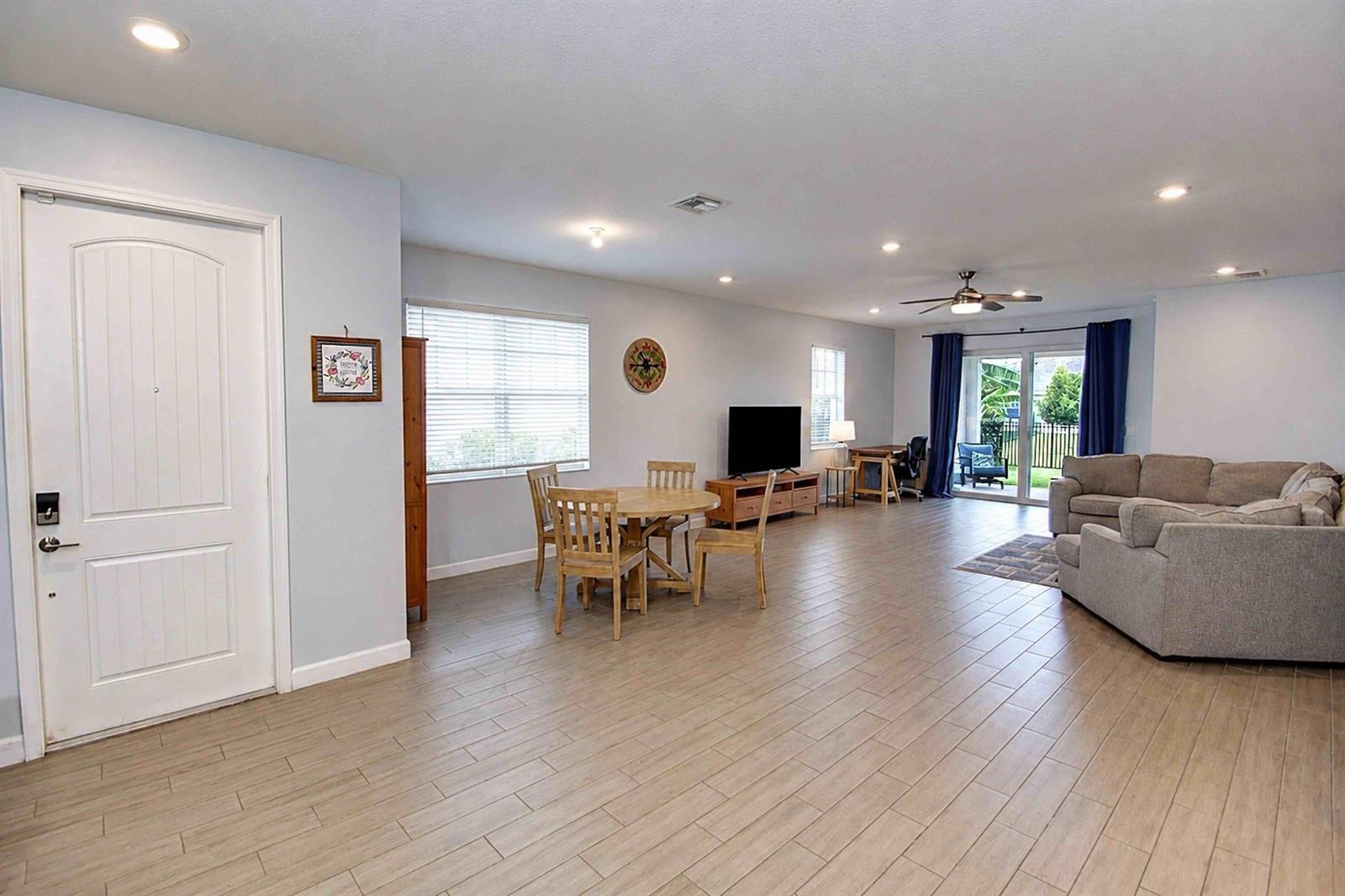 An open-concept living and dining area features light wood-look tile flooring and a sliding glass door — 1307 Tangled Orchard Trace, Loxahatchee FL 33470, LOXAHATCHEE, FL