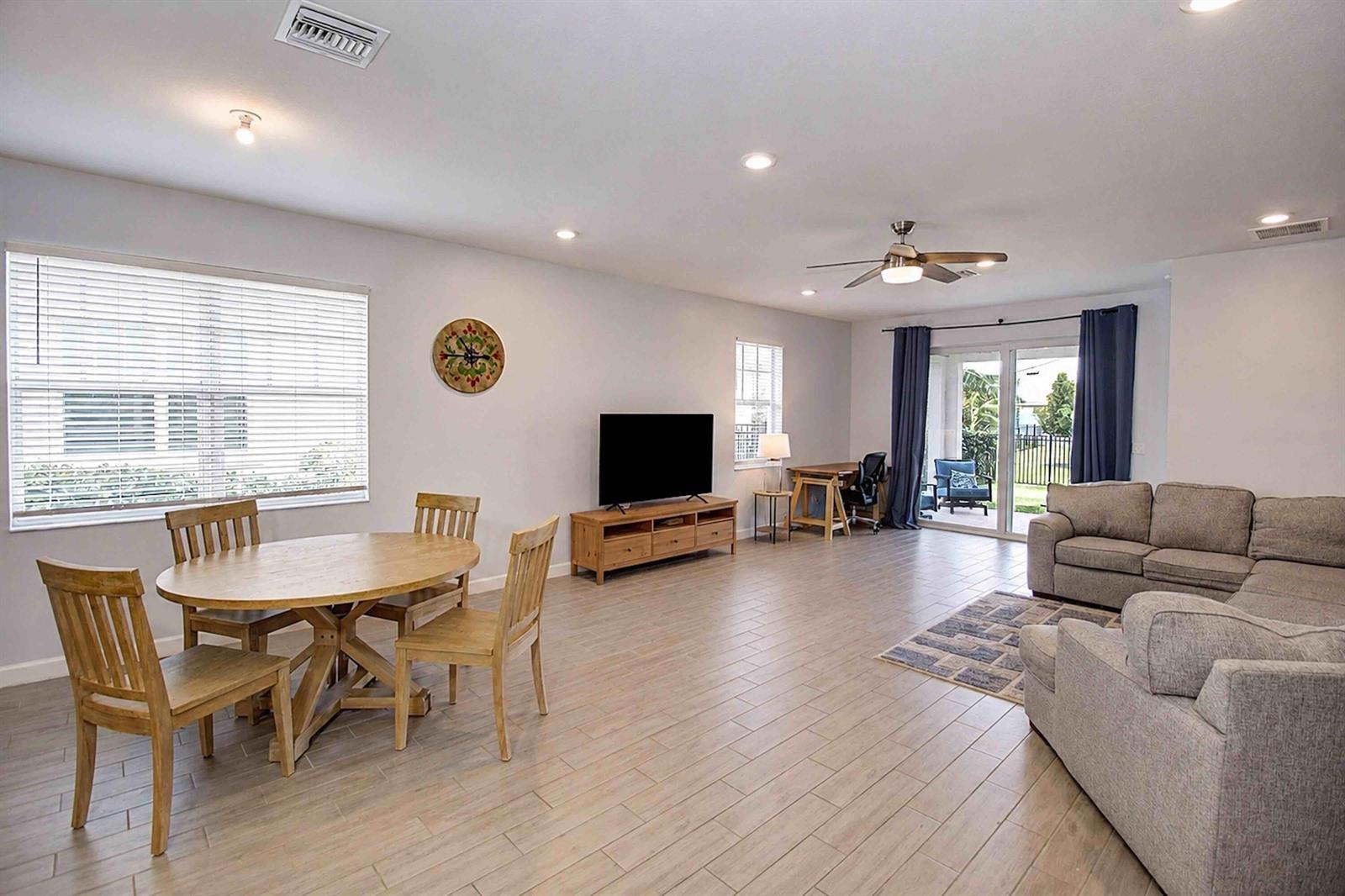 An open-concept living and dining area features tile flooring, a sectional sofa, and sliding doors — 1307 Tangled Orchard Trace, Loxahatchee FL 33470, LOXAHATCHEE, FL
