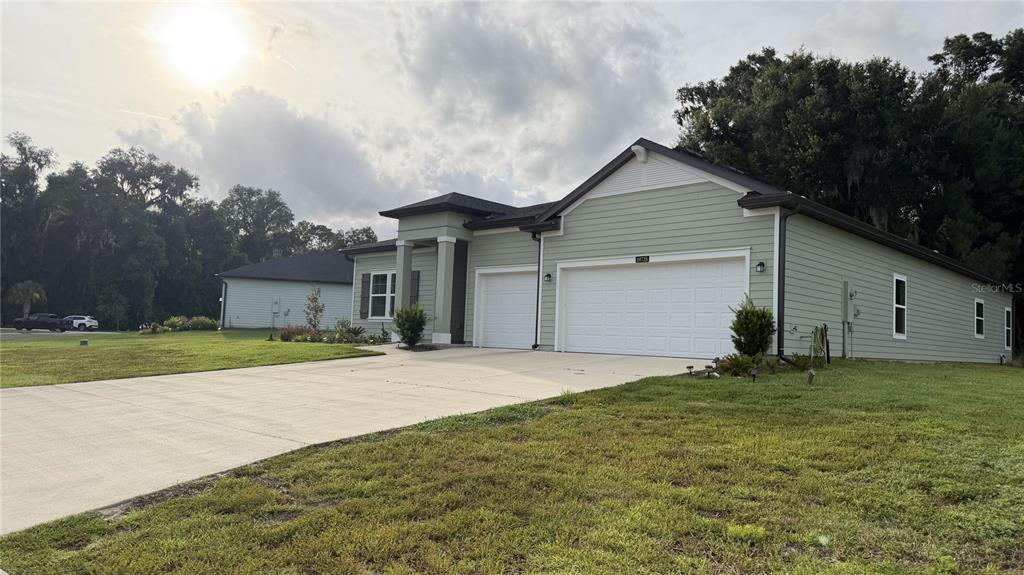 A light green single-story house features a three-car garage and a concrete driveway — 19725 SW 79TH PLACE, DUNNELLON, FL