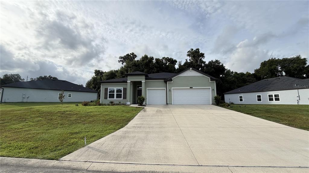 A light green single-story house with a three-car garage and a concrete driveway — 19725 SW 79TH PLACE, DUNNELLON, FL