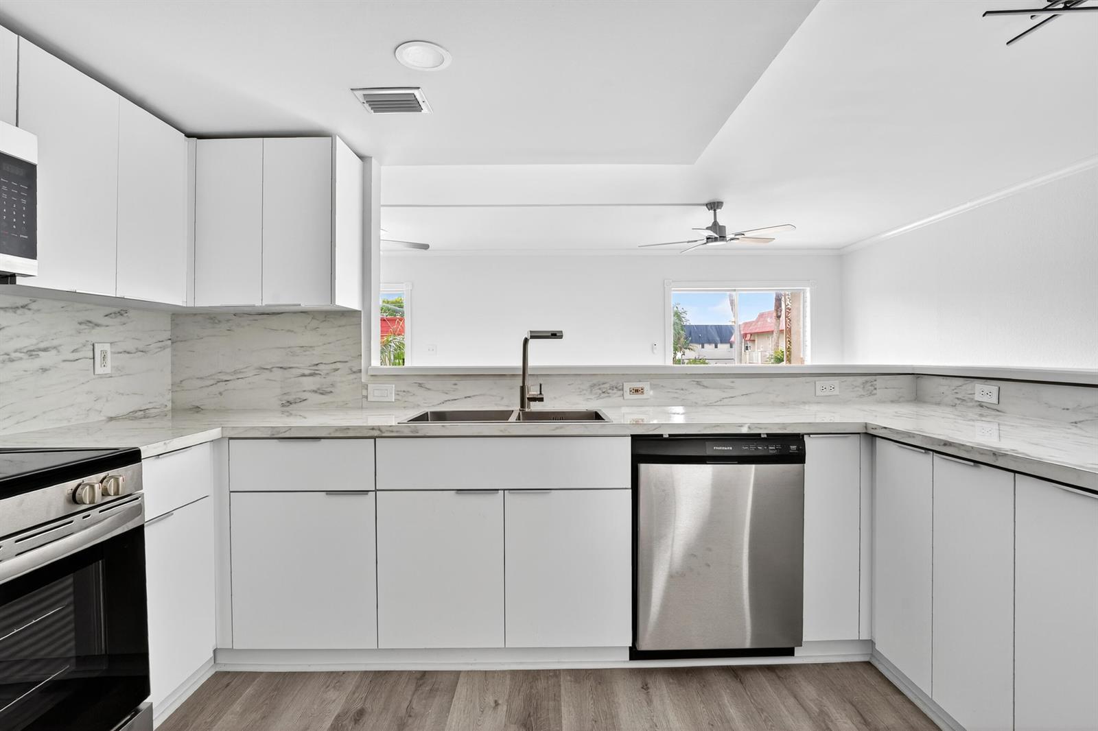 A modern kitchen features white cabinets, marble-look countertops, stainless steel appliances, and wood-look flooring — 495 SE 8th Street # 242, Deerfield Beach FL 33441, DEERFIELD BEACH, FL