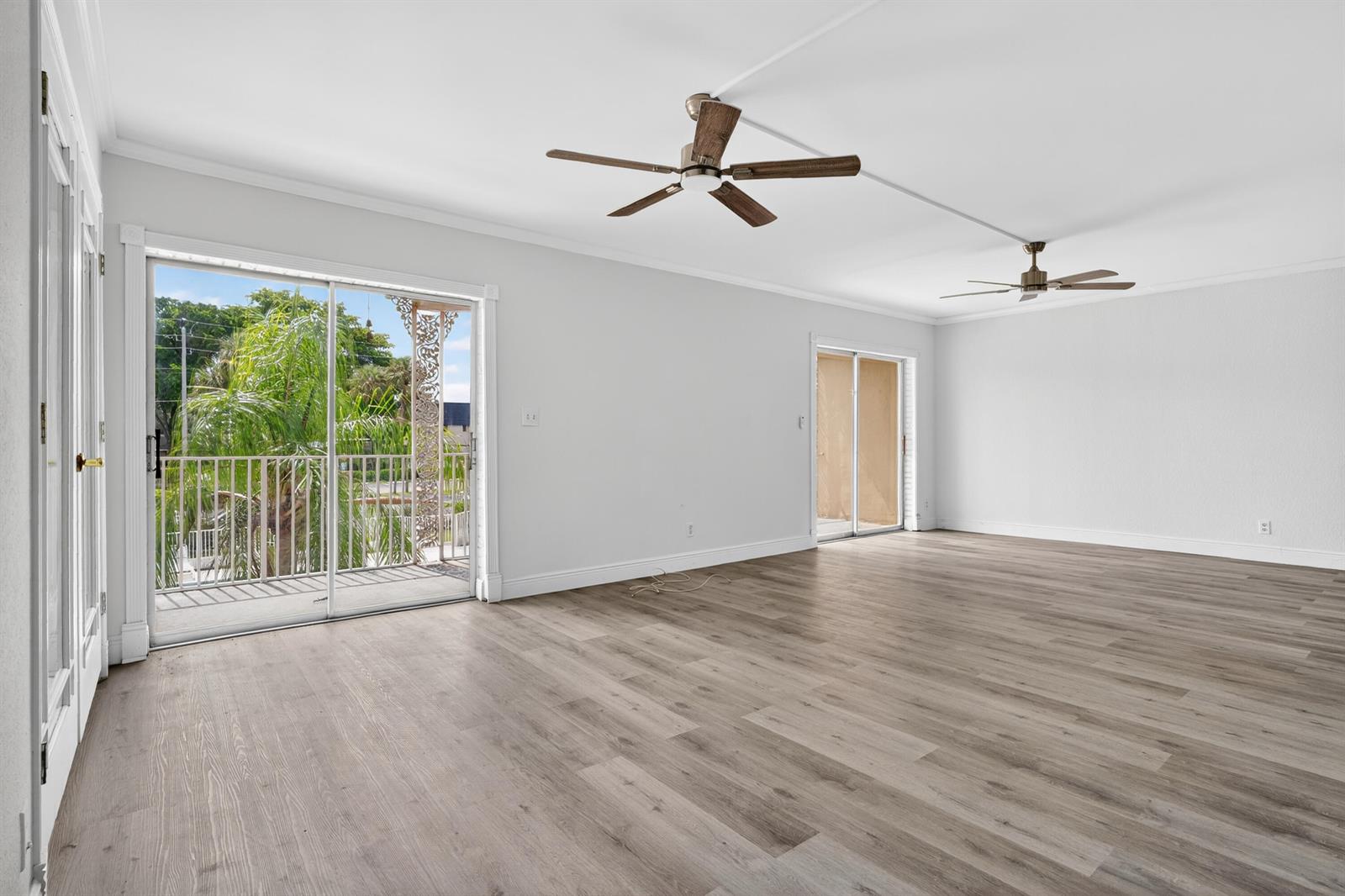 An empty room with light wood-look flooring, two ceiling fans, and sliding glass doors to balconies — 495 SE 8th Street # 242, Deerfield Beach FL 33441, DEERFIELD BEACH, FL