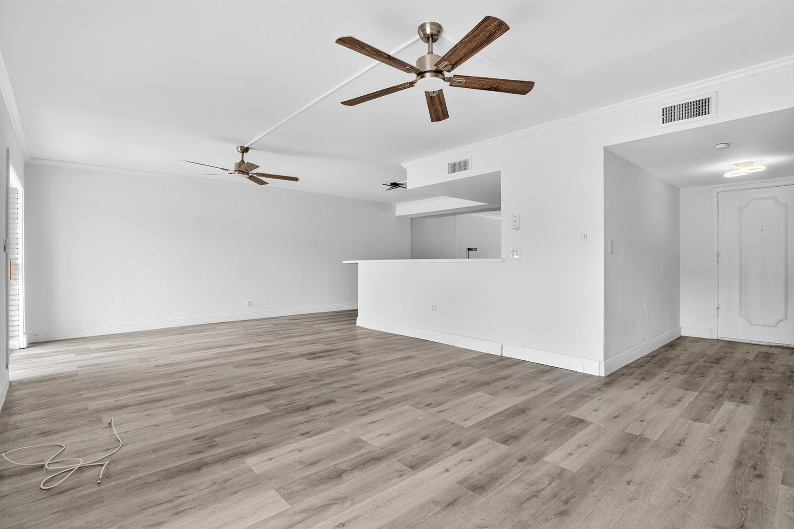 An empty room features light gray wood-look flooring, white walls, and two ceiling fans — 495 SE 8th Street # 242, Deerfield Beach FL 33441, DEERFIELD BEACH, FL