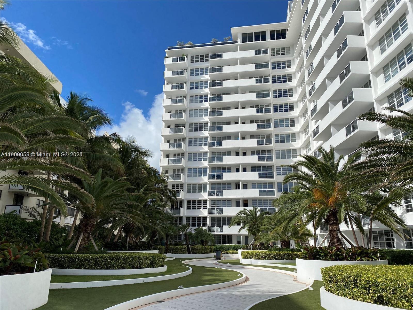 A white multi-story apartment building stands behind a landscaped courtyard with palm trees — 100 Lincoln Rd # 607, Miami Beach FL 33139, MIAMI BEACH, FL