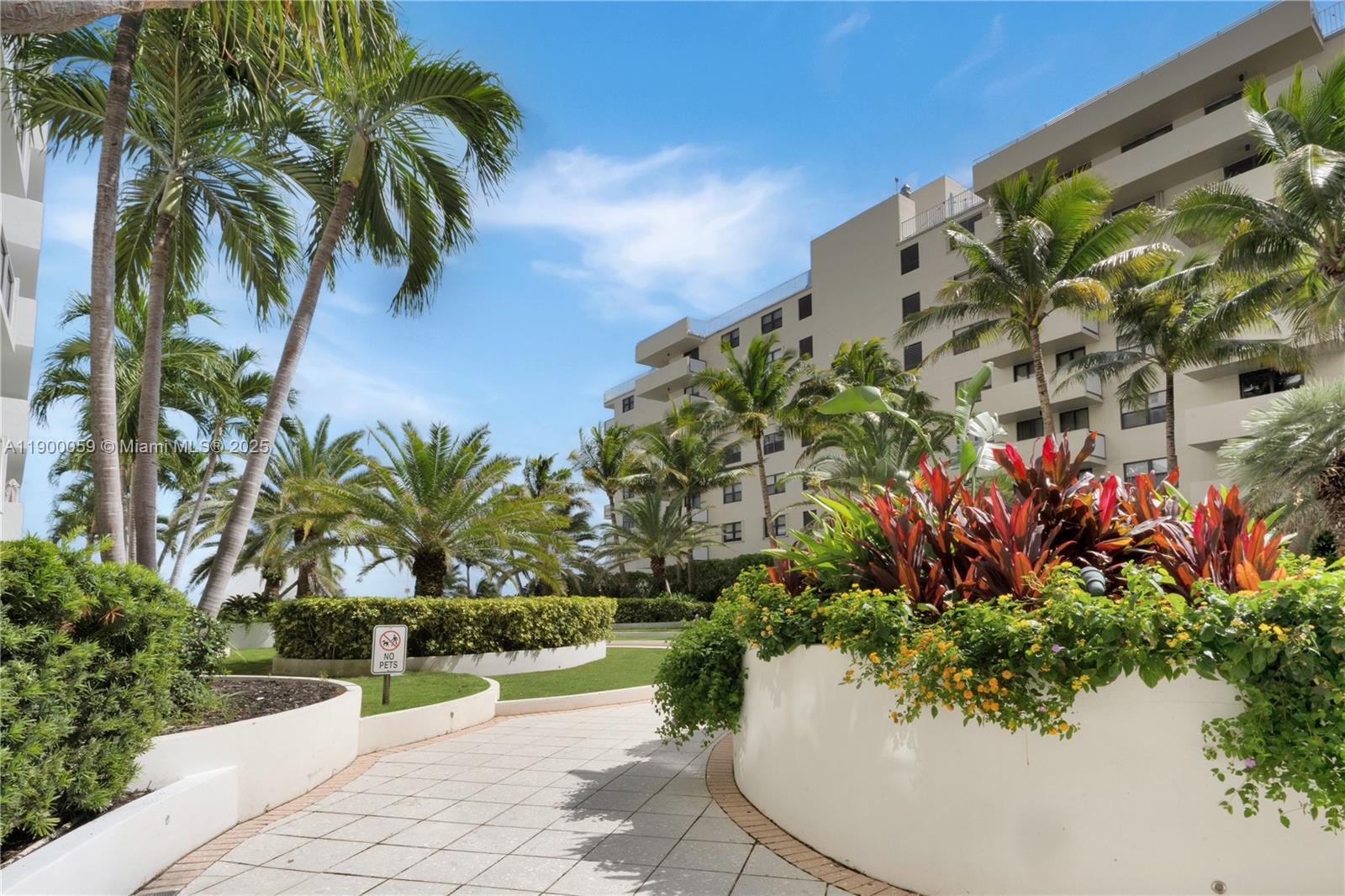A paved walkway leads through a landscaped courtyard with palm trees and a residential building — 100 Lincoln Rd # 607, Miami Beach FL 33139, MIAMI BEACH, FL