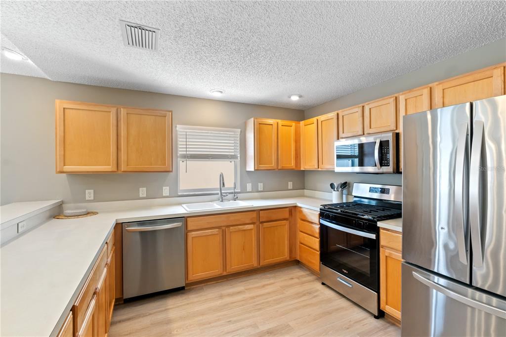 A kitchen features light wood cabinets, stainless steel appliances, and light-colored countertops — 1666 SUMMERCHASE LOOP, THE VILLAGES, FL