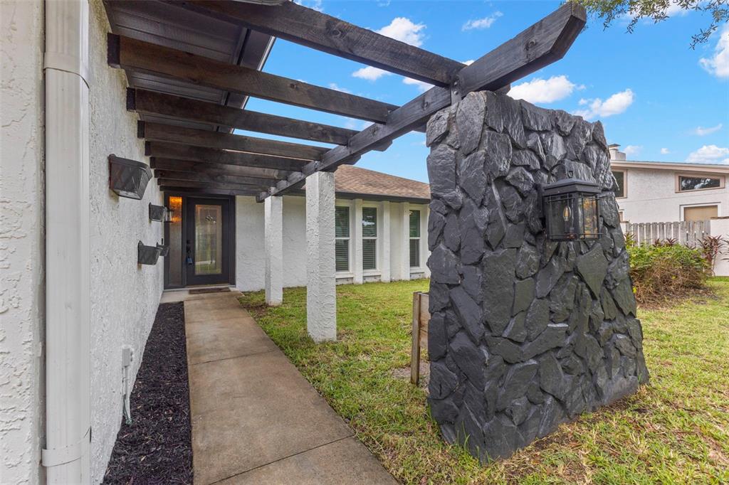 A walkway leads to a front door under a wooden pergola beside a stone wall — 3097 HAVERFORD DRIVE, CLEARWATER, FL