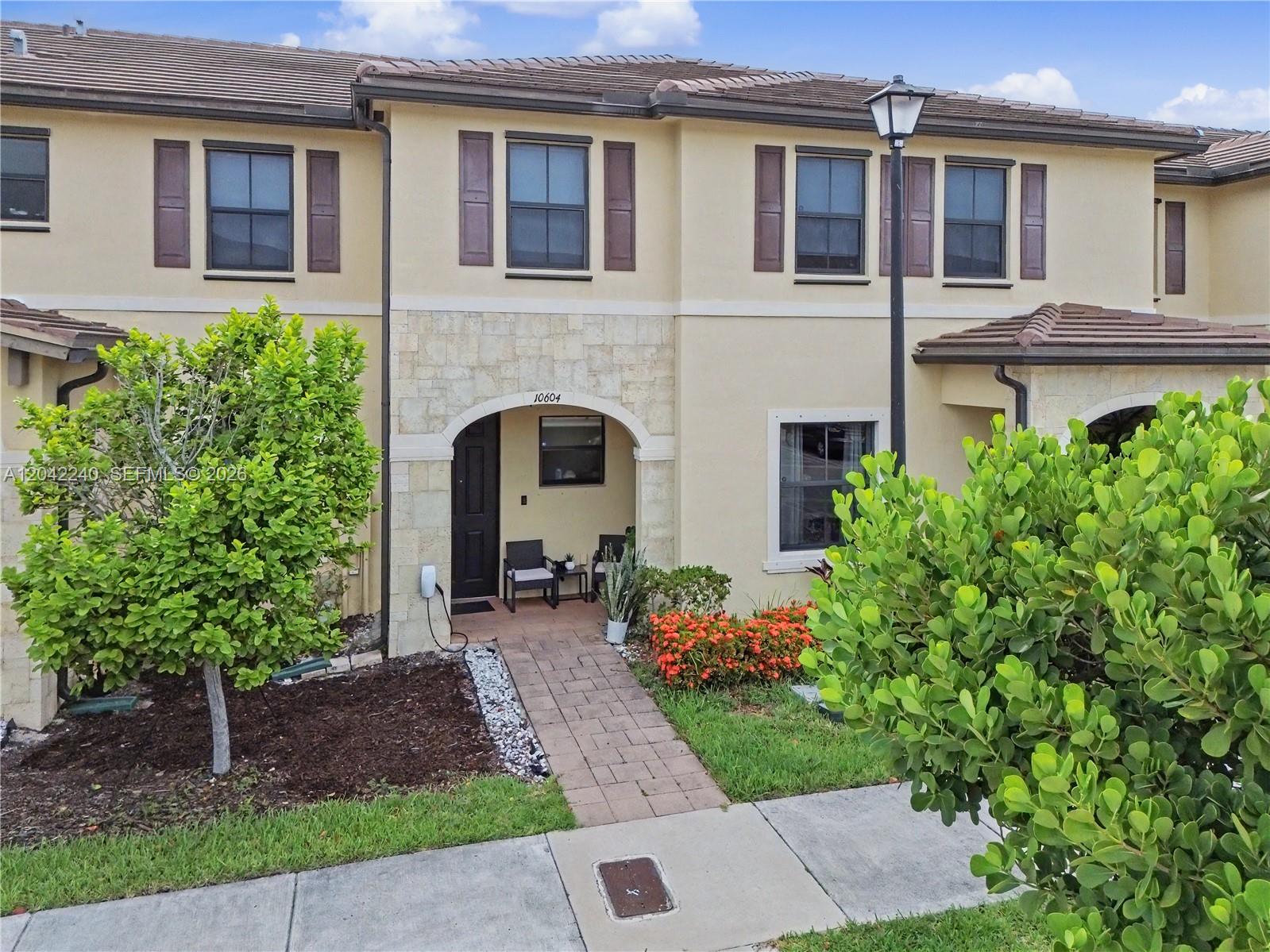 A two-story townhouse exterior features a stone-accented entryway, brown shutters, and a paved walkway — 10604 W 33rd Ln, Hialeah FL 33018, HIALEAH, FL