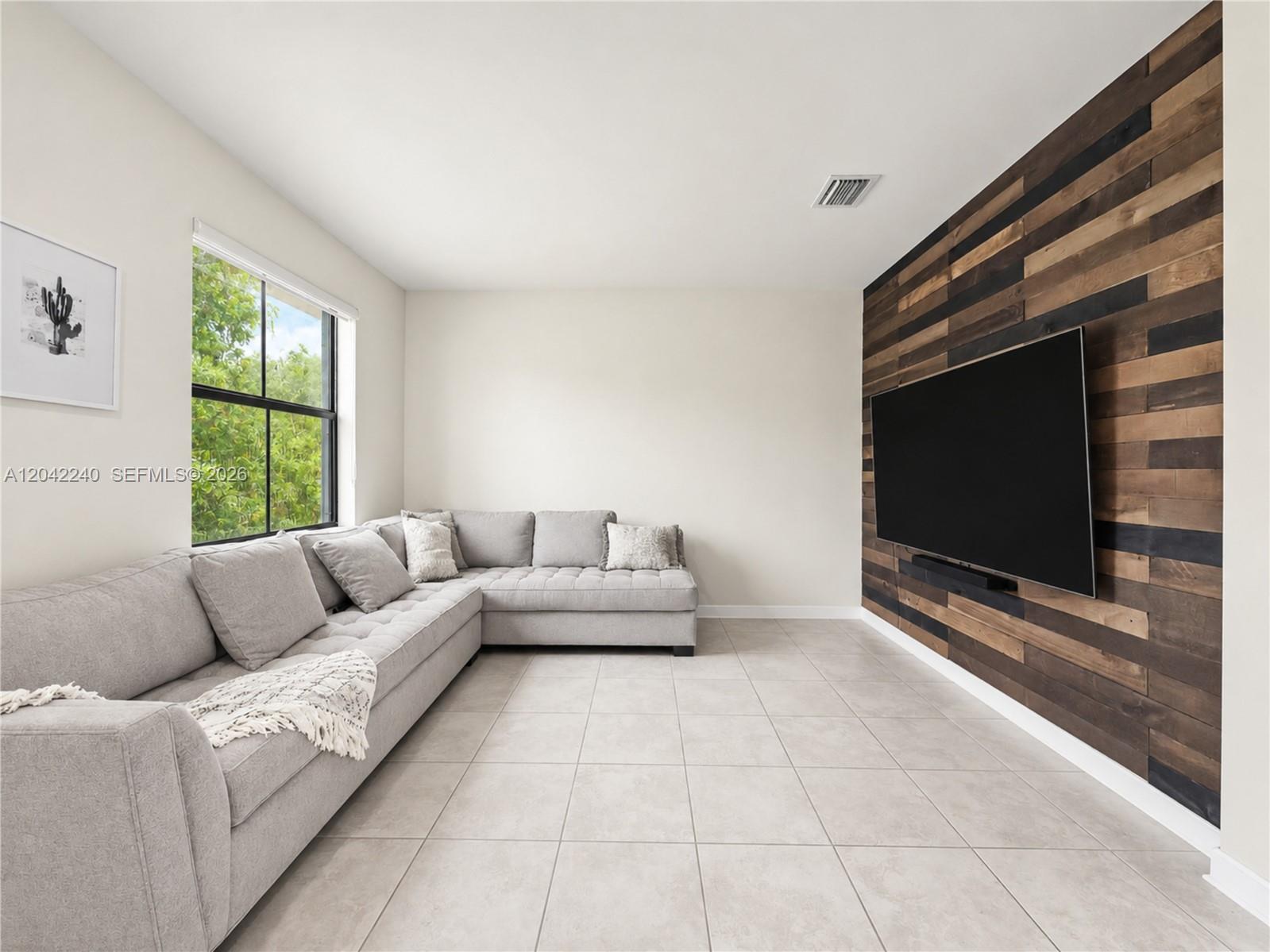 A living room features a gray sectional sofa, tiled floors, and a wood-paneled accent wall — 10604 W 33rd Ln, Hialeah FL 33018, HIALEAH, FL