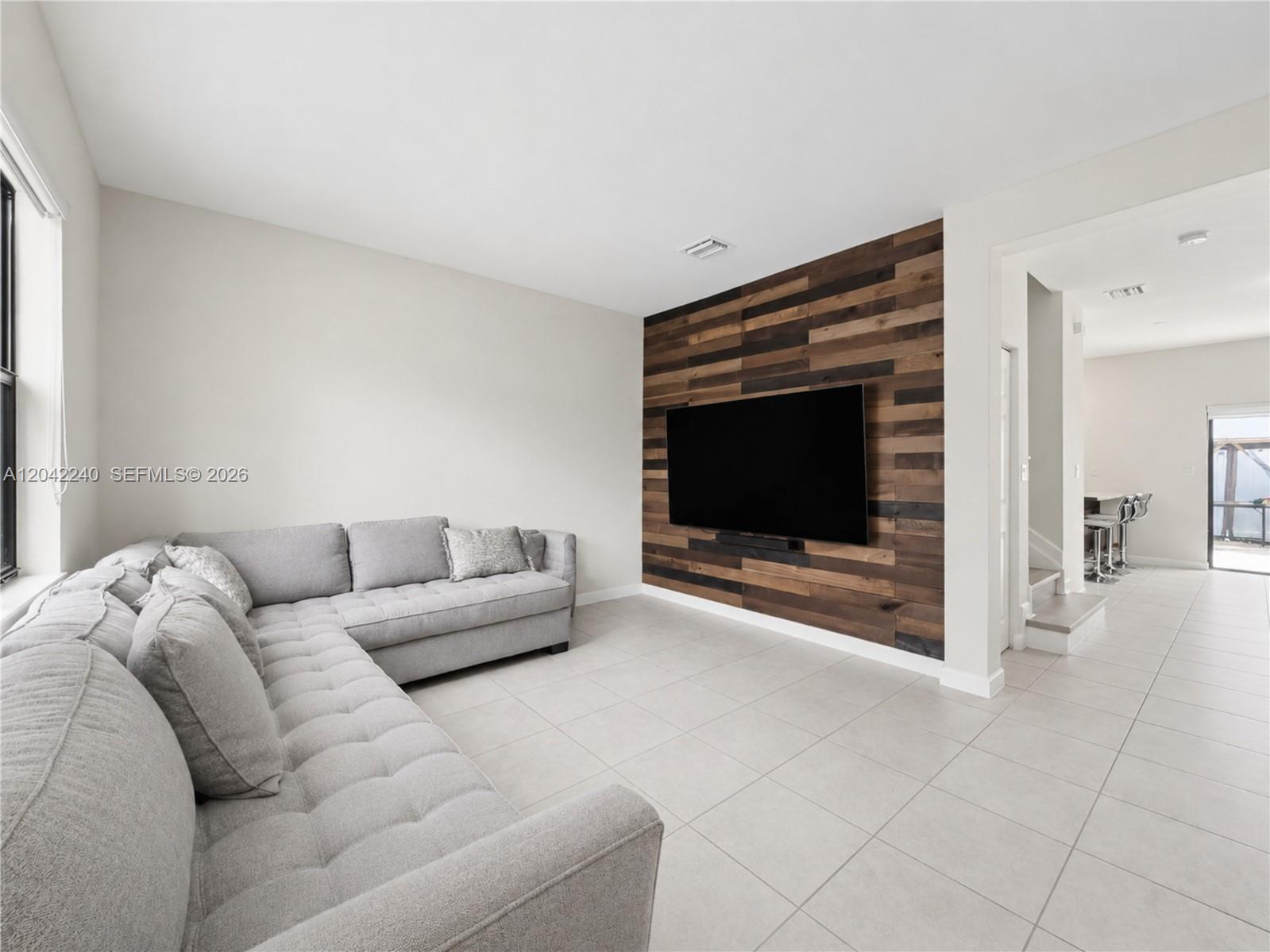 A living room features a grey sectional sofa, tile flooring, and a wood-paneled accent wall — 10604 W 33rd Ln, Hialeah FL 33018, HIALEAH, FL