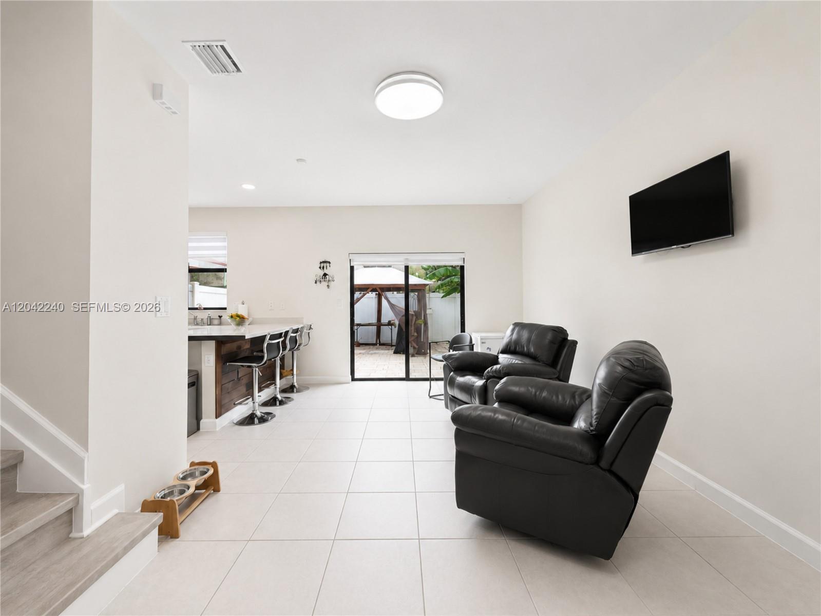 A living area with tile floors, two black leather recliners, and a kitchen breakfast bar — 10604 W 33rd Ln, Hialeah FL 33018, HIALEAH, FL