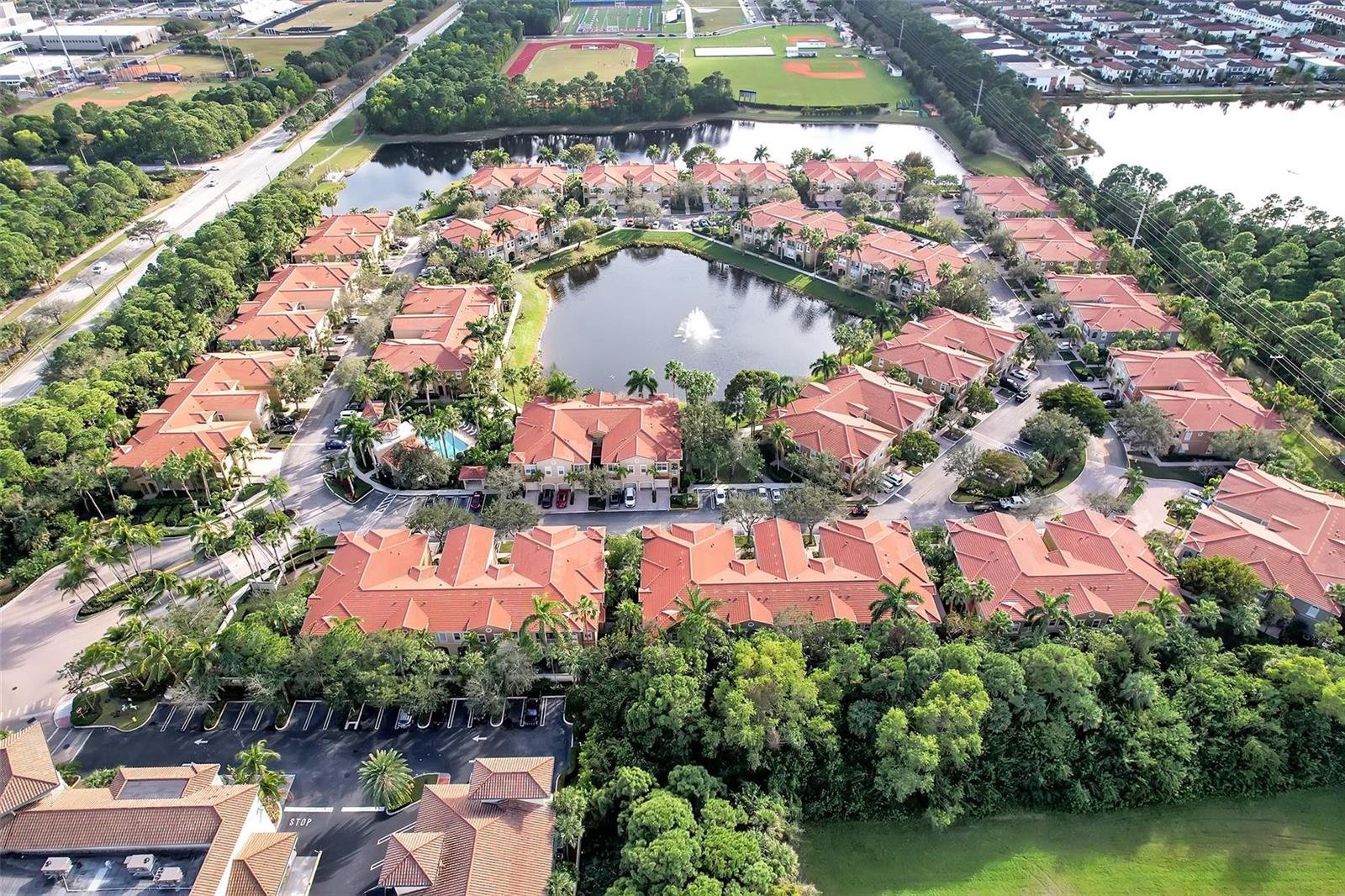 An aerial view of a residential complex with red-tiled roofs surrounding a central pond — 4941 E Bonsai Circle E # 209, Palm Beach Gardens FL 33418, PALM BEACH GARDENS, FL