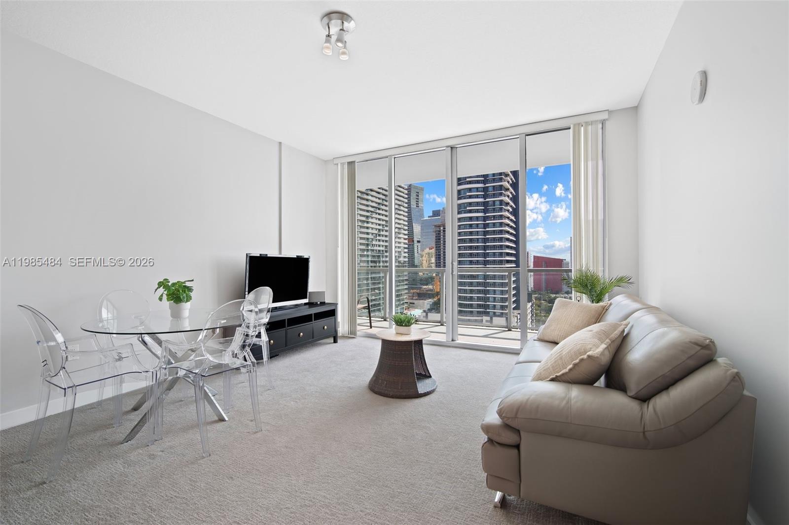 A living and dining area features a beige sofa, glass table, and floor-to-ceiling windows — 79 SW 12th St, Miami FL 33130, MIAMI, FL