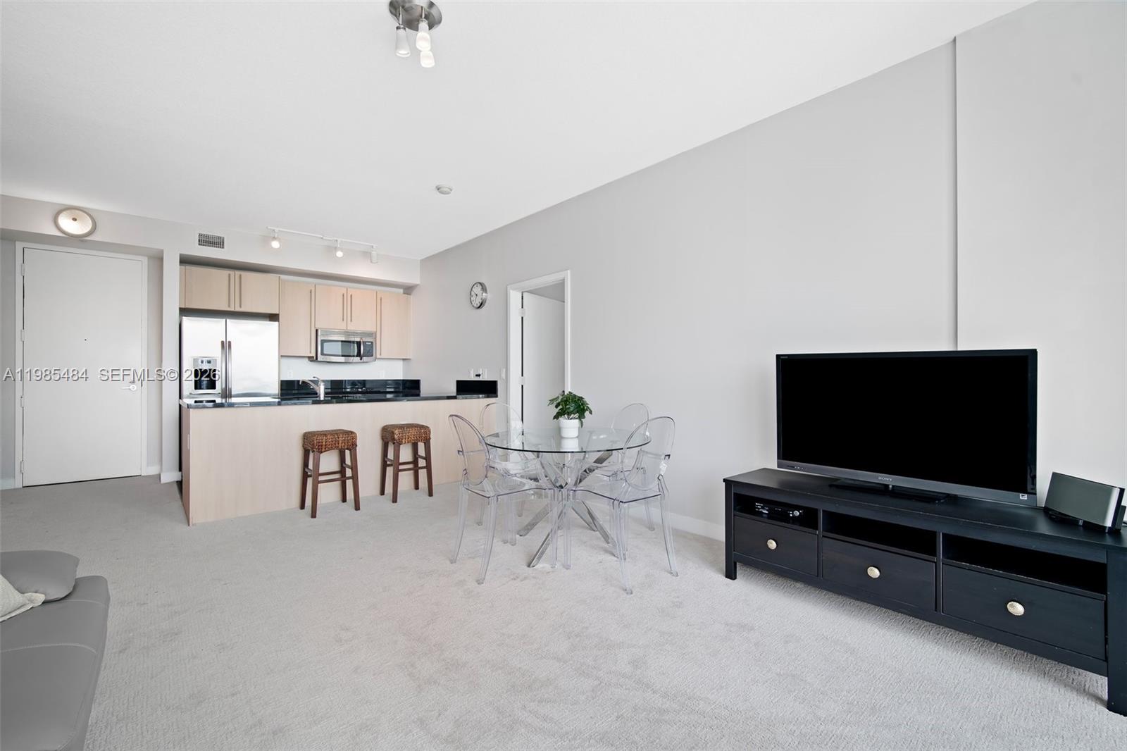 An open-concept living and dining area features a kitchen with light wood cabinets and carpet — 79 SW 12th St, Miami FL 33130, MIAMI, FL
