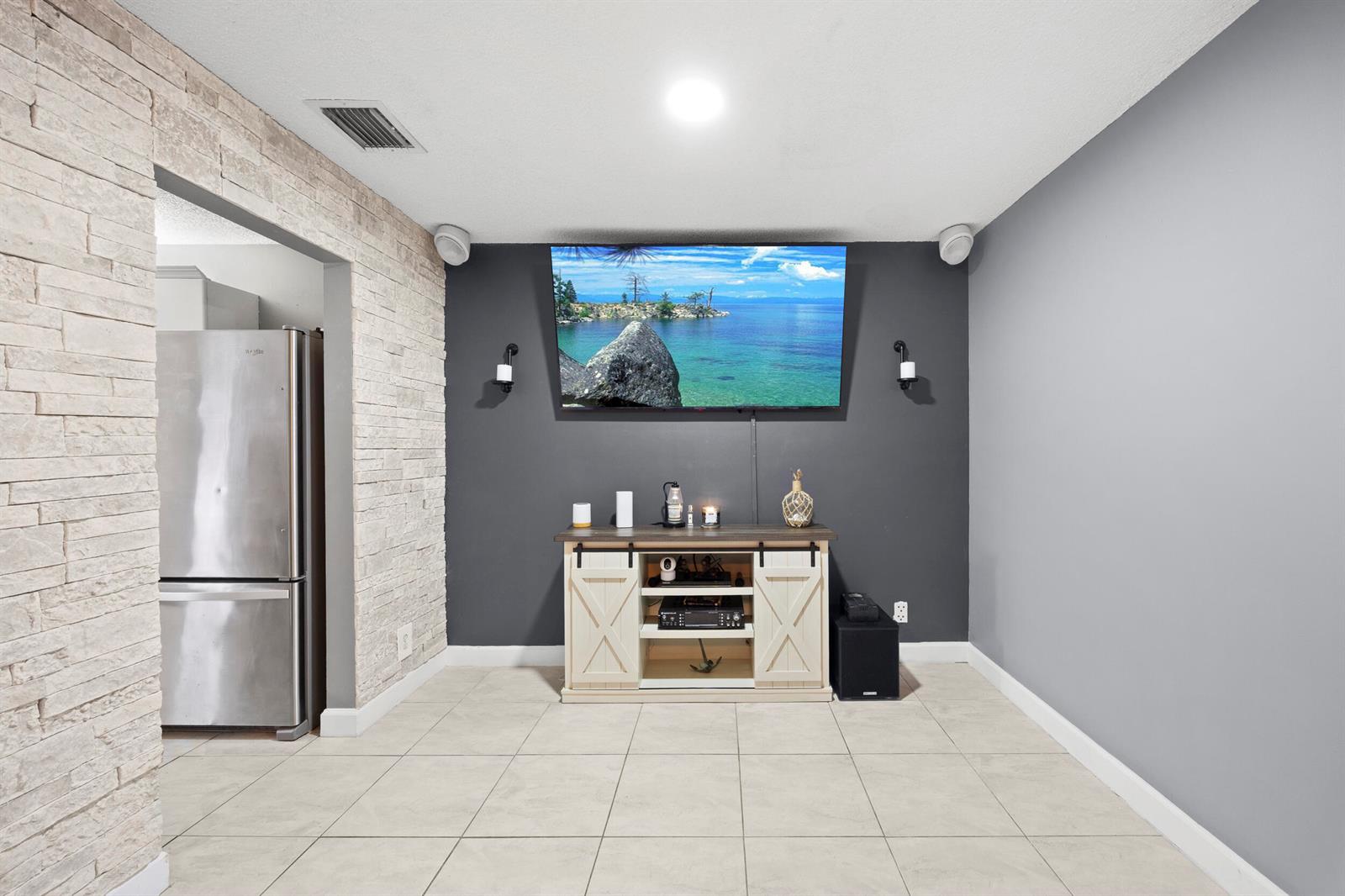 A living room features a wall-mounted television, a media console, and a stone-accented wall — 1928 Discovery Circle E, Deerfield Beach FL 33442, DEERFIELD BEACH, FL