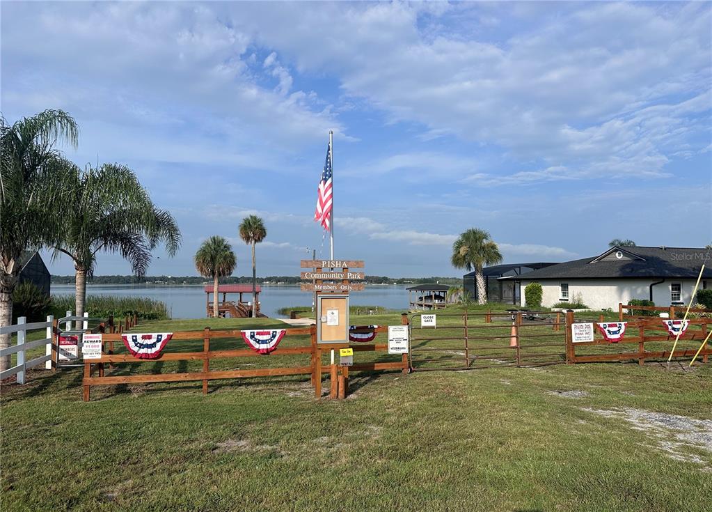 A wooden fence surrounds a waterfront community park with a flag pole and boat dock — 5216 SYDNEY ROAD, FRUITLAND PARK, FL