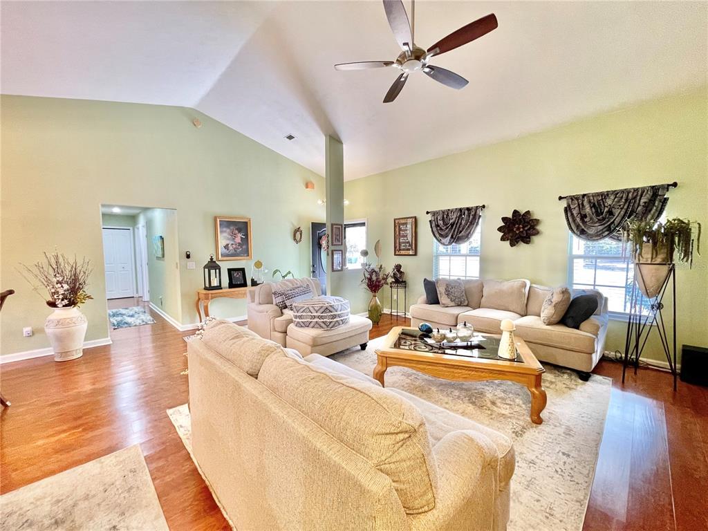 A living room with light green walls, vaulted ceilings, hardwood floors, and two beige sofas — 25336 SW 22ND AVENUE, NEWBERRY, FL