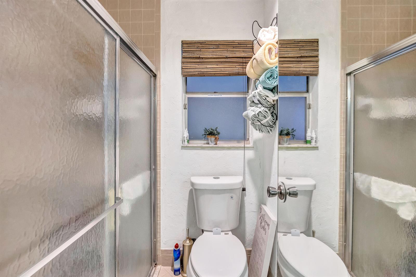 A bathroom features a toilet, a glass-enclosed shower, and a window with a bamboo shade — 6137 Rainbow Circle, FL 33463, FL