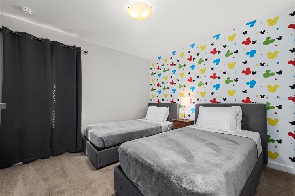 A bedroom features two twin beds and an accent wall with colorful Mickey Mouse patterns — 4402 LE REVE COURT, KISSIMMEE, FL