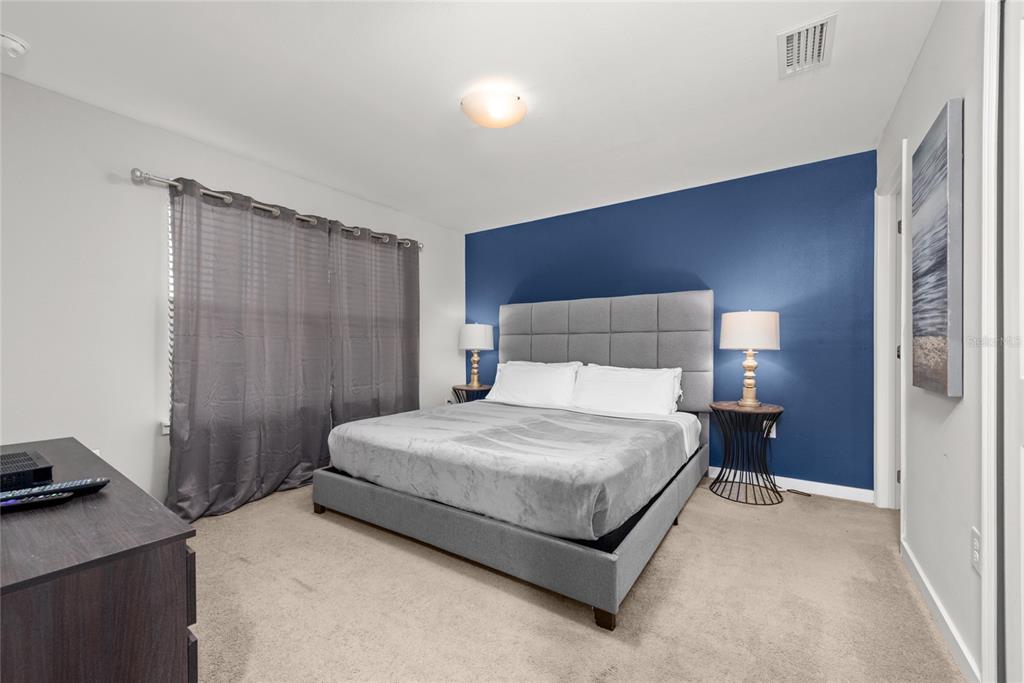 A bedroom features a grey upholstered bed against a blue accent wall with two lamps — 4402 LE REVE COURT, KISSIMMEE, FL