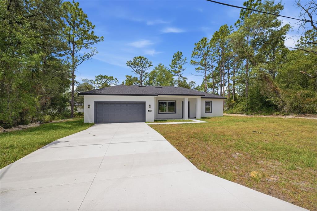 A single-story house with a white exterior, gray garage door, and a concrete driveway — 3428 W CUSHION DRIVE, CITRUS SPRINGS, FL