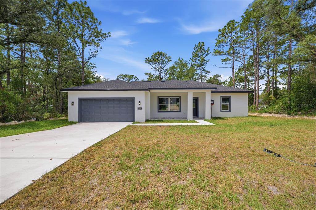 A single-story house with a gray garage door, white exterior, and a concrete driveway — 3428 W CUSHION DRIVE, CITRUS SPRINGS, FL