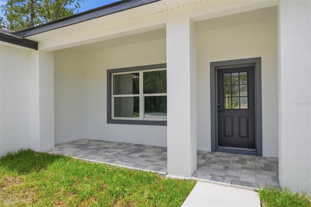 A covered entryway features a paved porch, white stucco walls, and a dark front door — 3428 W CUSHION DRIVE, CITRUS SPRINGS, FL