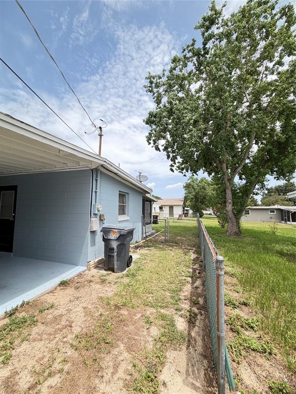 A side view of a light blue concrete block house with a trash bin and fence — 5 MOONLIGHT LANE, WINTER HAVEN, FL