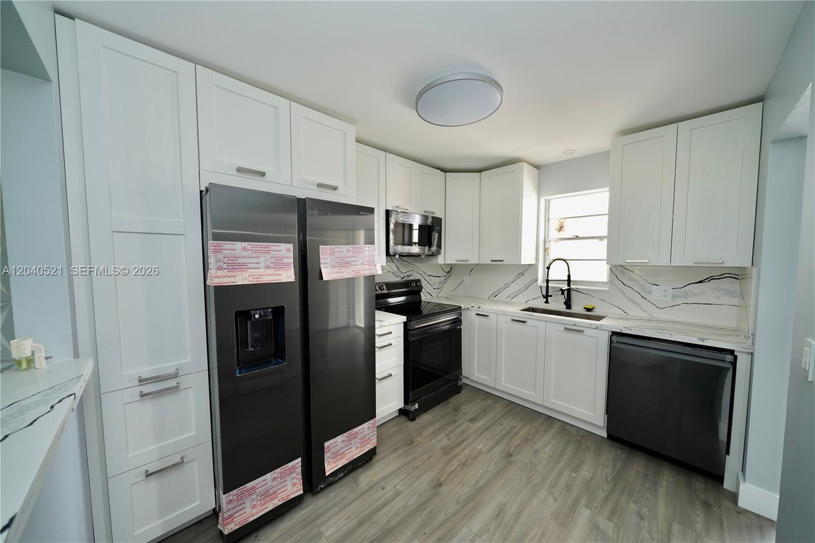 A kitchen features white cabinets, black appliances, and a marble-patterned backsplash with gray flooring — 2541 Aragon Blvd # 305, Sunrise FL 33322, SUNRISE, FL