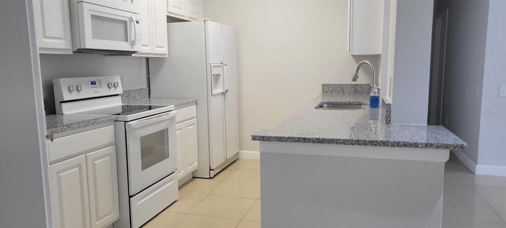 A kitchen features white cabinets, granite countertops, white appliances, and light-colored tile flooring — 7147 YACHT BASIN AVENUE UNIT 114, ORLANDO, FL