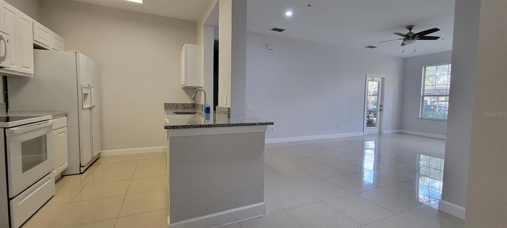 A kitchen with white cabinets and granite countertops opens into a tiled living area — 7147 YACHT BASIN AVENUE UNIT 114, ORLANDO, FL