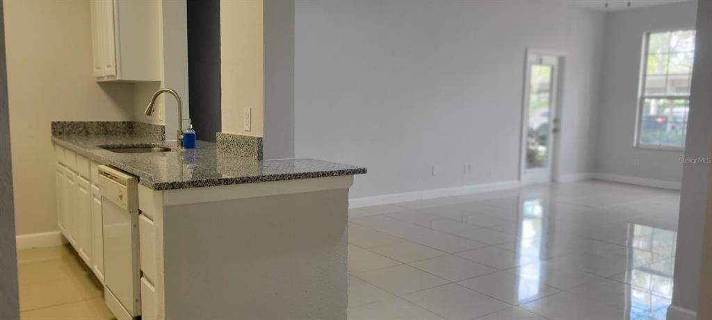 A kitchen with granite countertops and white cabinets overlooks a bright, tiled living area — 7147 YACHT BASIN AVENUE UNIT 114, ORLANDO, FL
