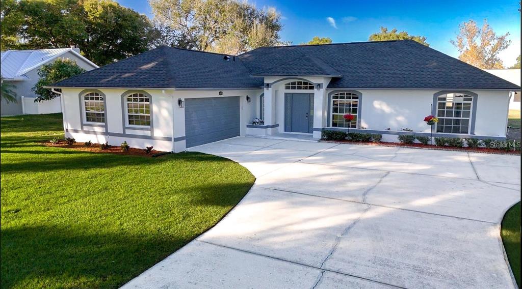 A single-story house with a white stucco exterior, gray roof, and a concrete driveway — 10711 LAKE HILL DRIVE, CLERMONT, FL