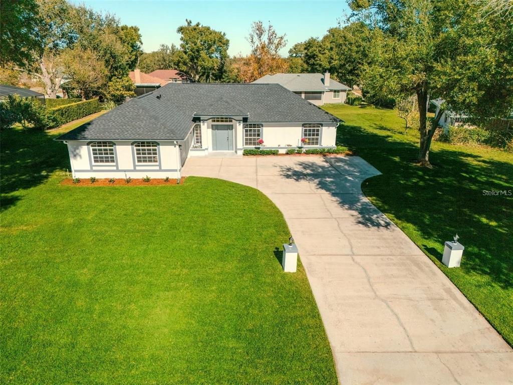 An aerial view shows a single-story white house with a dark roof and concrete driveway — 10711 LAKE HILL DRIVE, CLERMONT, FL