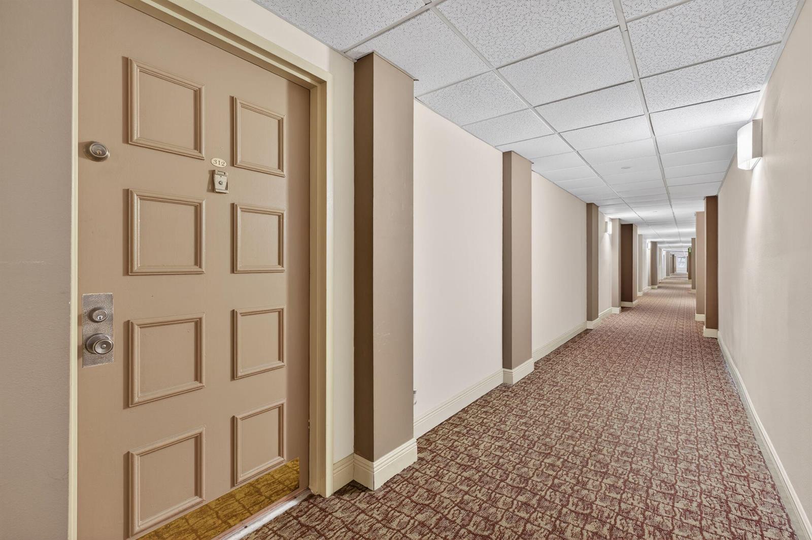 A long hotel hallway features a tan door labeled 312, patterned carpet, and recessed lighting — 1009 N Ocean Boulevard # 312, Pompano Beach FL 33062, POMPANO BEACH, FL