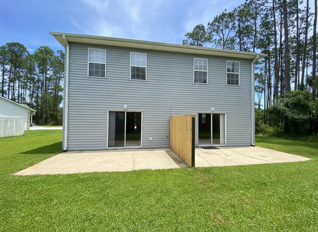 The exterior rear view of a two-story duplex features sliding glass doors and a concrete patio — 23 REGENT LANE UNIT A&B, PALM COAST, FL