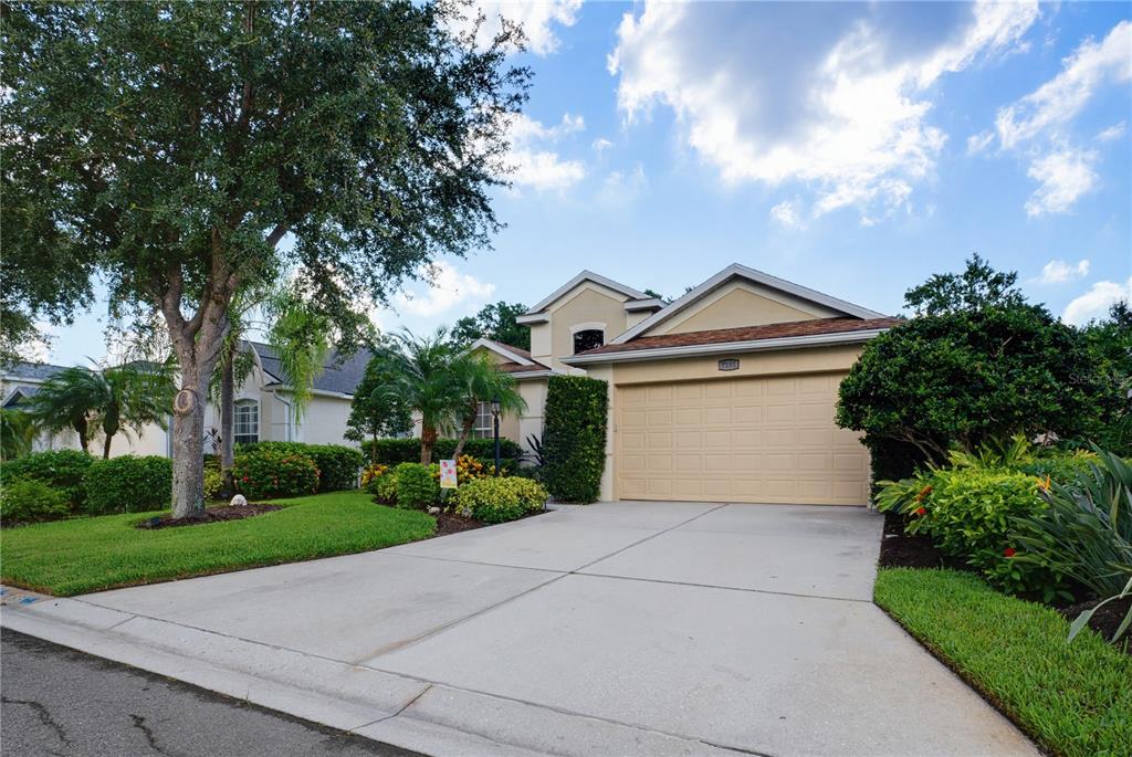 A single-story suburban house with a beige garage, concrete driveway, and lush landscaping — 7155 SPIKERUSH COURT, BRADENTON, FL
