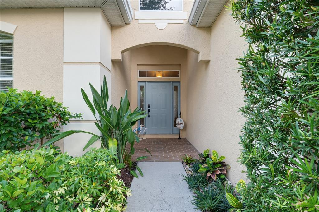 A light blue front door is centered under a covered entryway with brick flooring — 7155 SPIKERUSH COURT, BRADENTON, FL